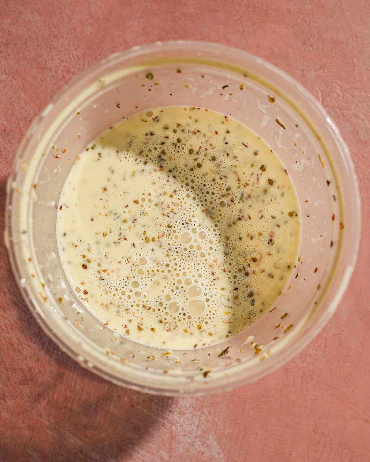 Creamy Italian-style dressing with herbs and spices in clear container.