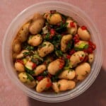 Marinated white bean salad with herbs, peppers, and dressing in a container.