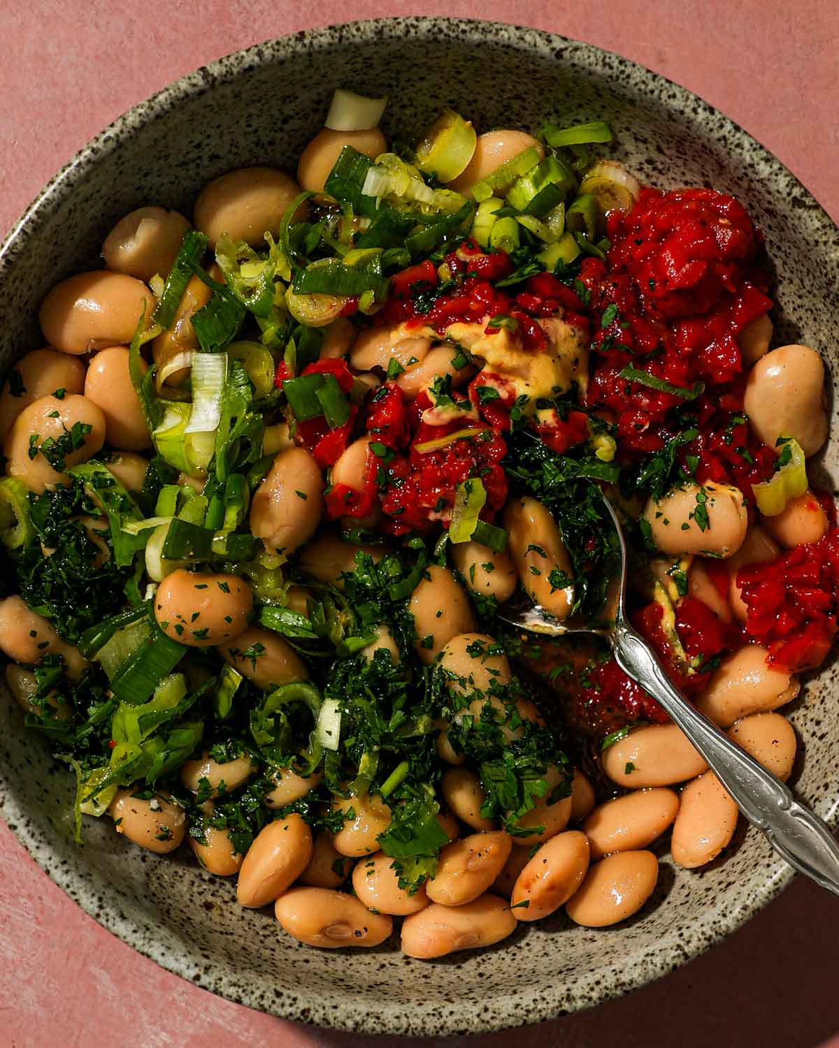 Bowl of beans topped with scallions, peppers, parsley, and mustard before mixing.