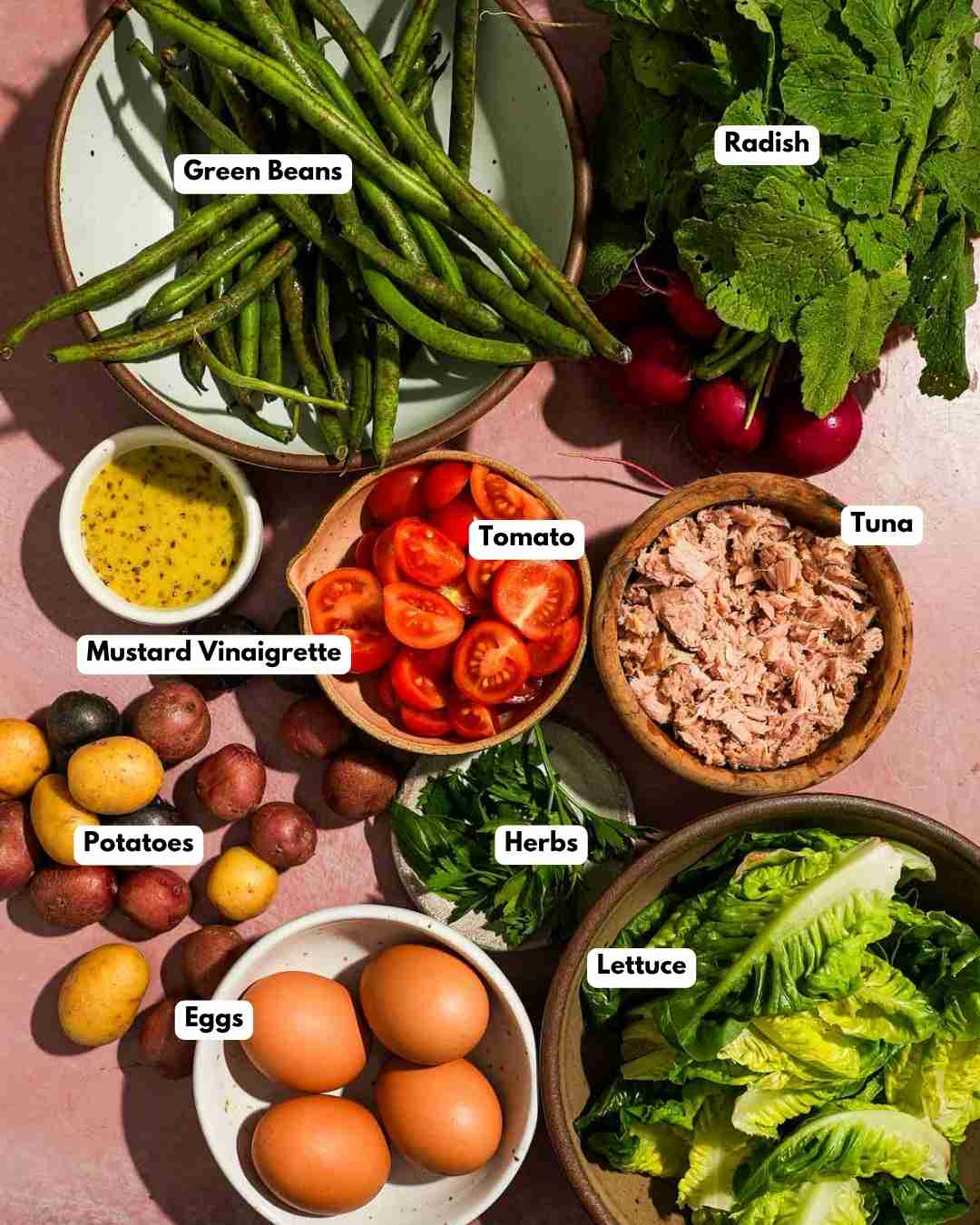 Ingredients laid out on a pink background to make a tuna nicoise salad.