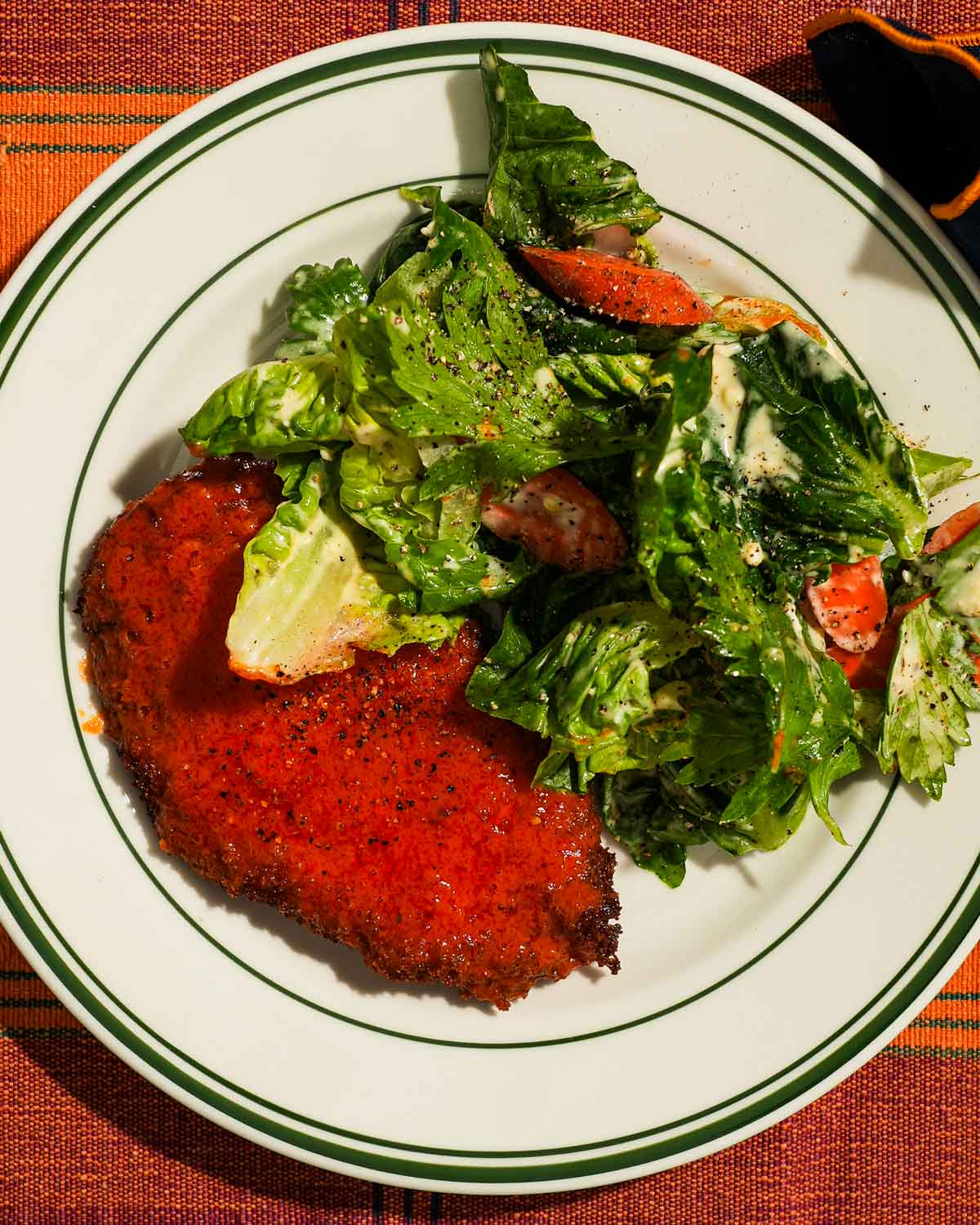 Plate of buffalo chicken cutlet with green salad topped in creamy dressing.