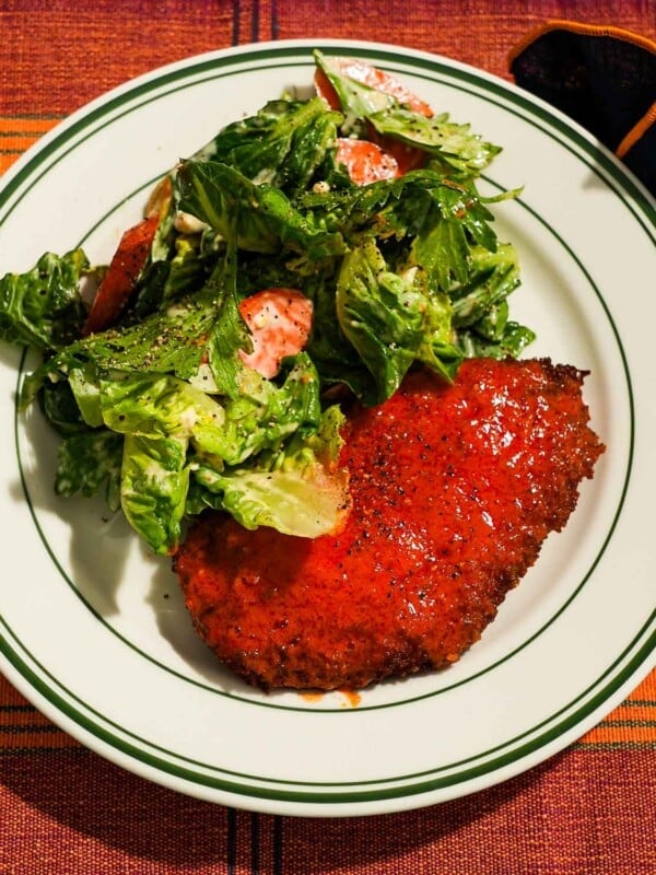Buffalo chicken cutlet alongside dressed salad with cracked pepper garnish.