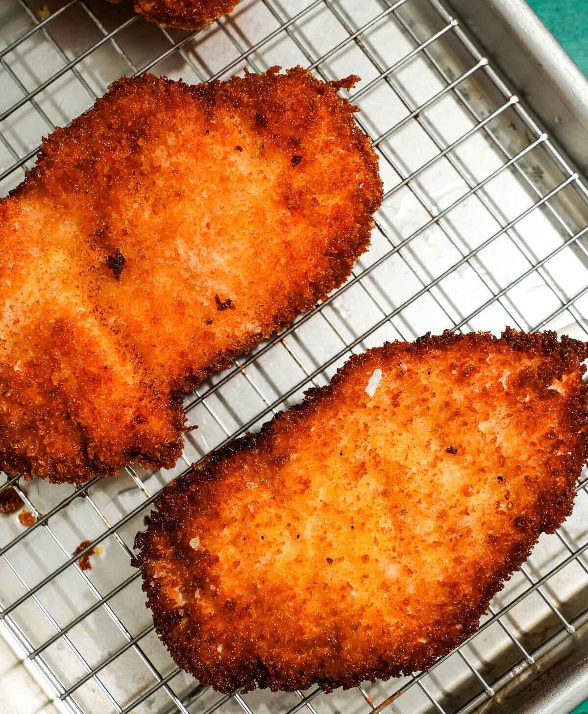 Golden fried chicken cutlets cooling on wire rack after frying.