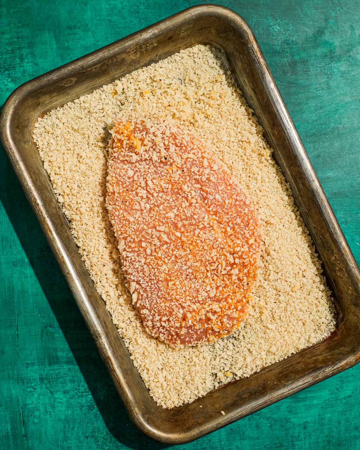 Breaded chicken breast resting in panko crumbs before frying.