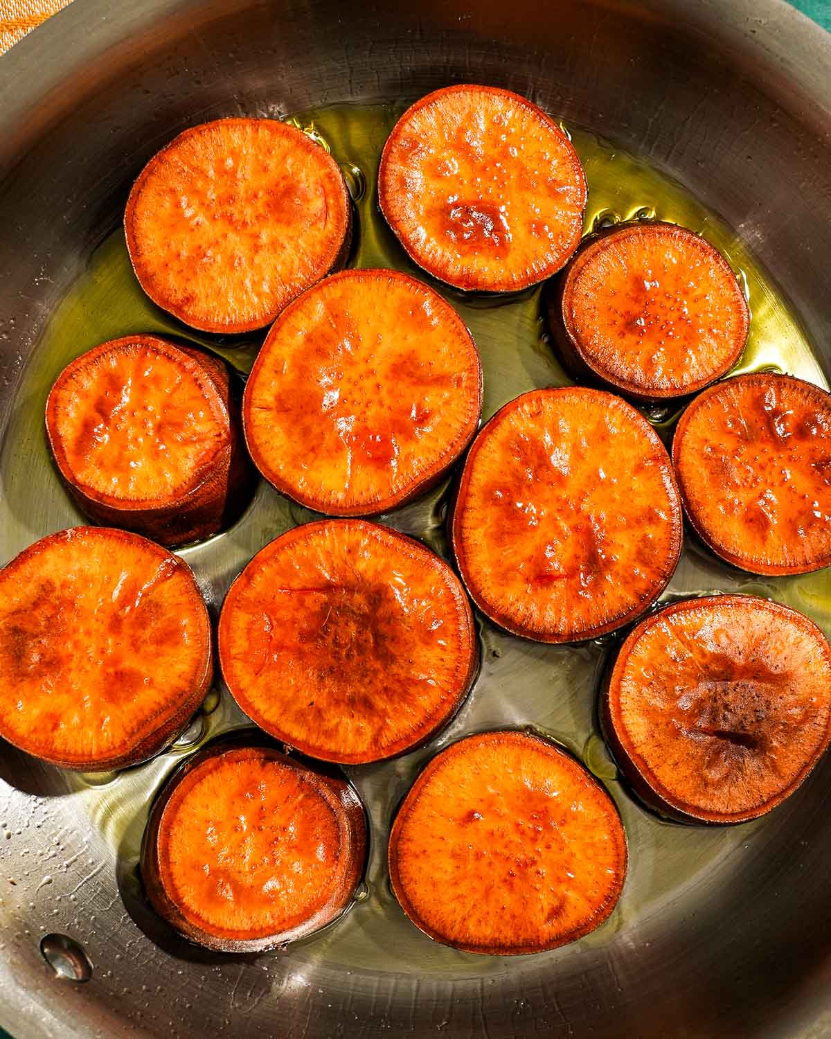A skillet of sweet potato rounds being seared.