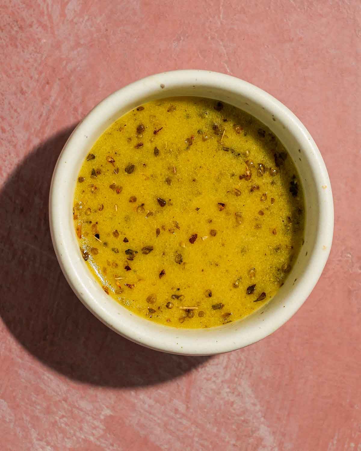 Mustard Dijon vinaigrette in a small bowl on a pink background.