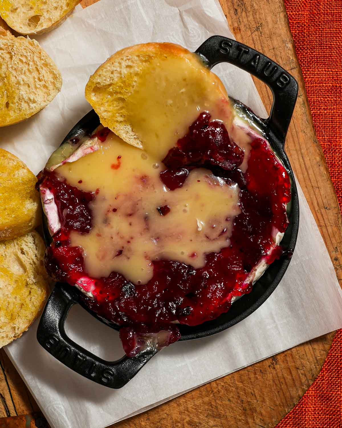 A small baking dish with baked brie with a crostini and cranberry sauce.
