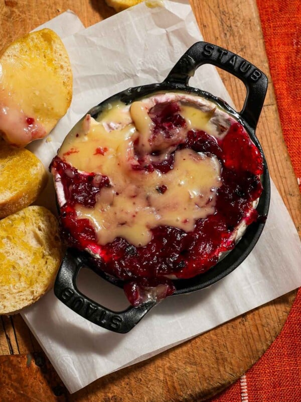 A baking dish of melty baked brie cheese with cranberry sauce.