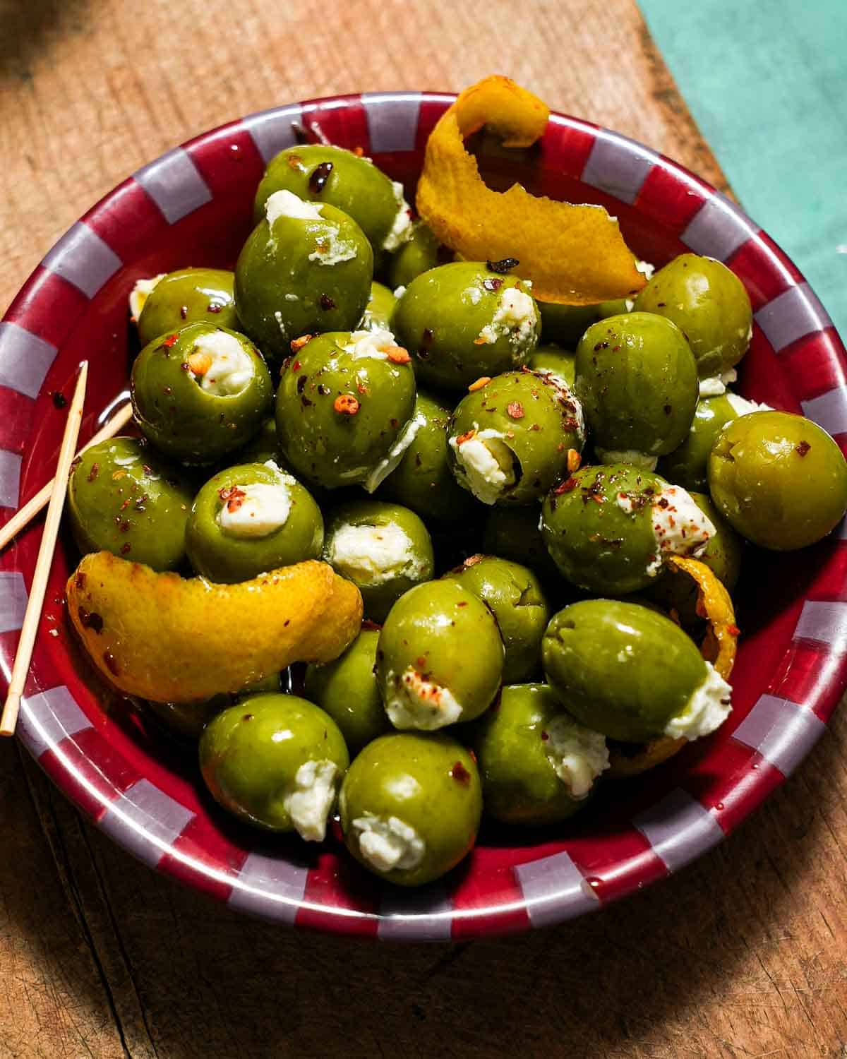 A small mixing bowl of stuffed blue cheese green olives on a cutting board.