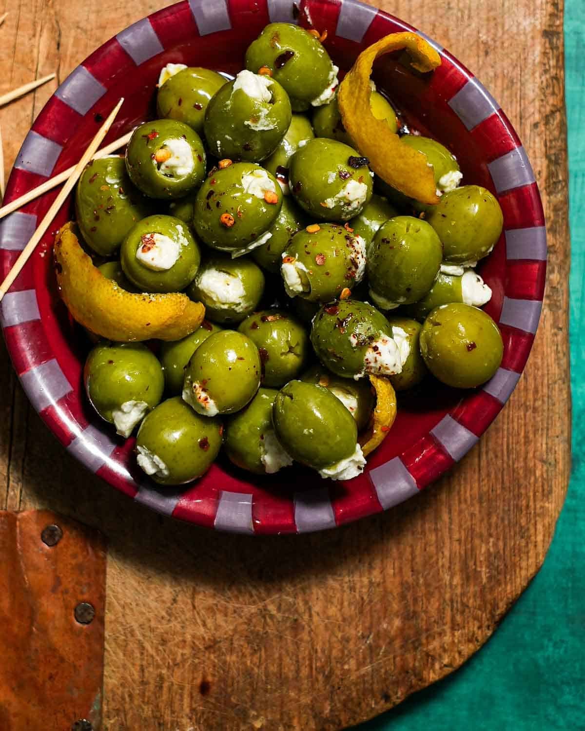 A bowl of blue cheese stuffed olives on a cutting board with toothpicks.