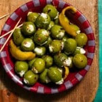 A bowl of blue cheese stuffed olives on a cutting board with toothpicks.