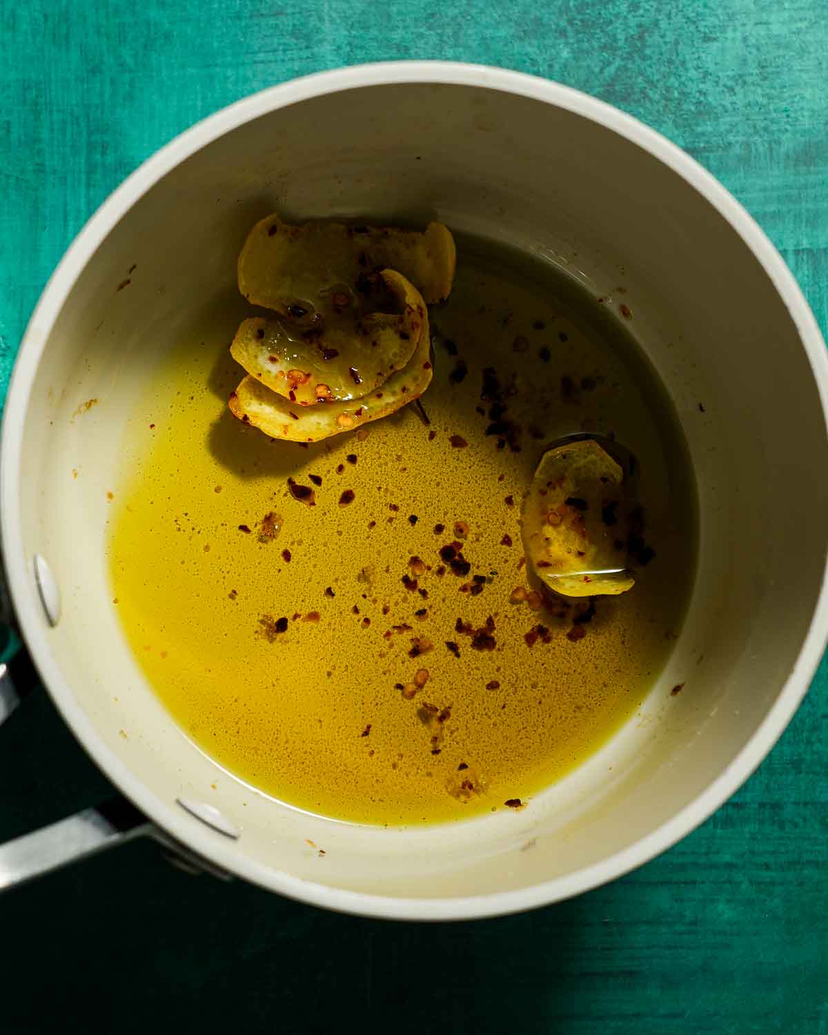 A pot of infused olive oil with lemon peel and chili flakes.