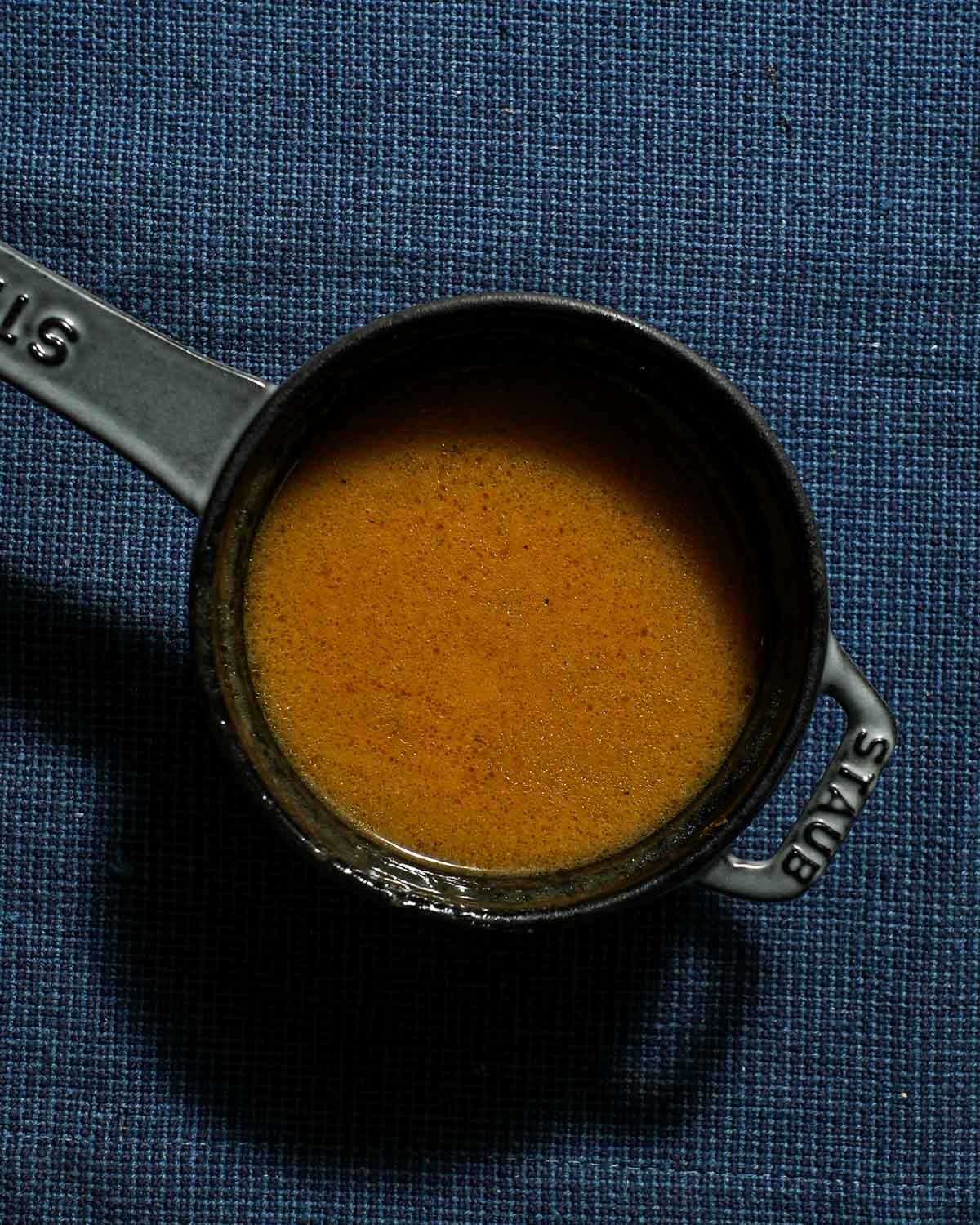 A small pot of chicken gravy on a blue tablecloth.