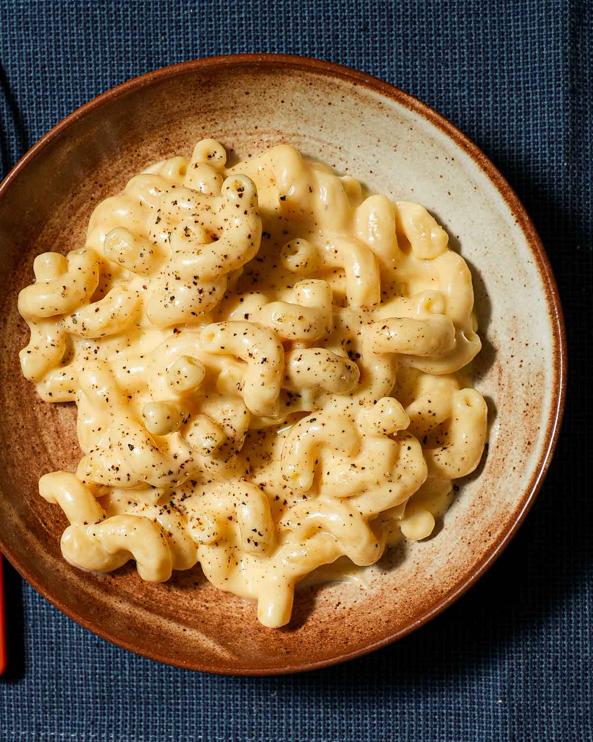 A plated bowl of creamy macaroni and cheese on a blue linen.