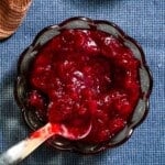 A bowl of jalapeno cranberry sauce with a spoon on a blue tablecloth.