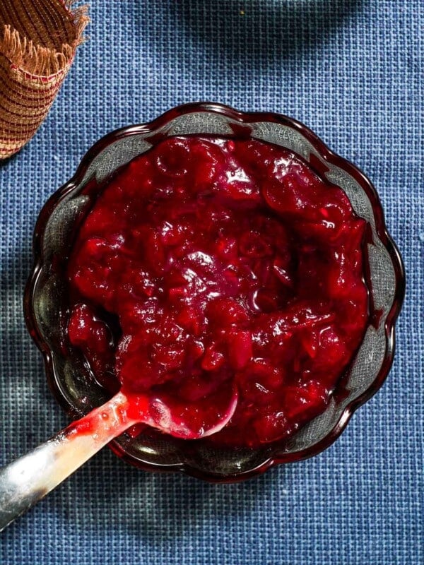 A bowl of jalapeno cranberry sauce with a spoon on a blue tablecloth.