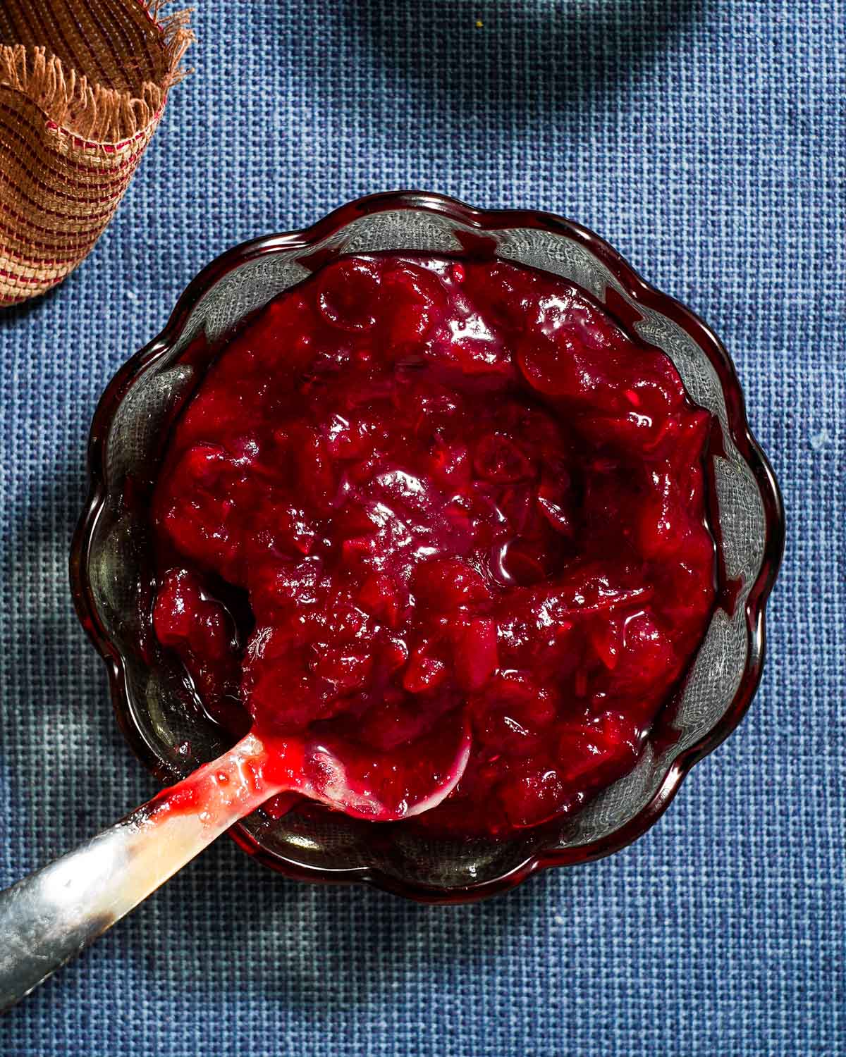 A bowl of jalapeno cranberry sauce with a spoon on a blue tablecloth.