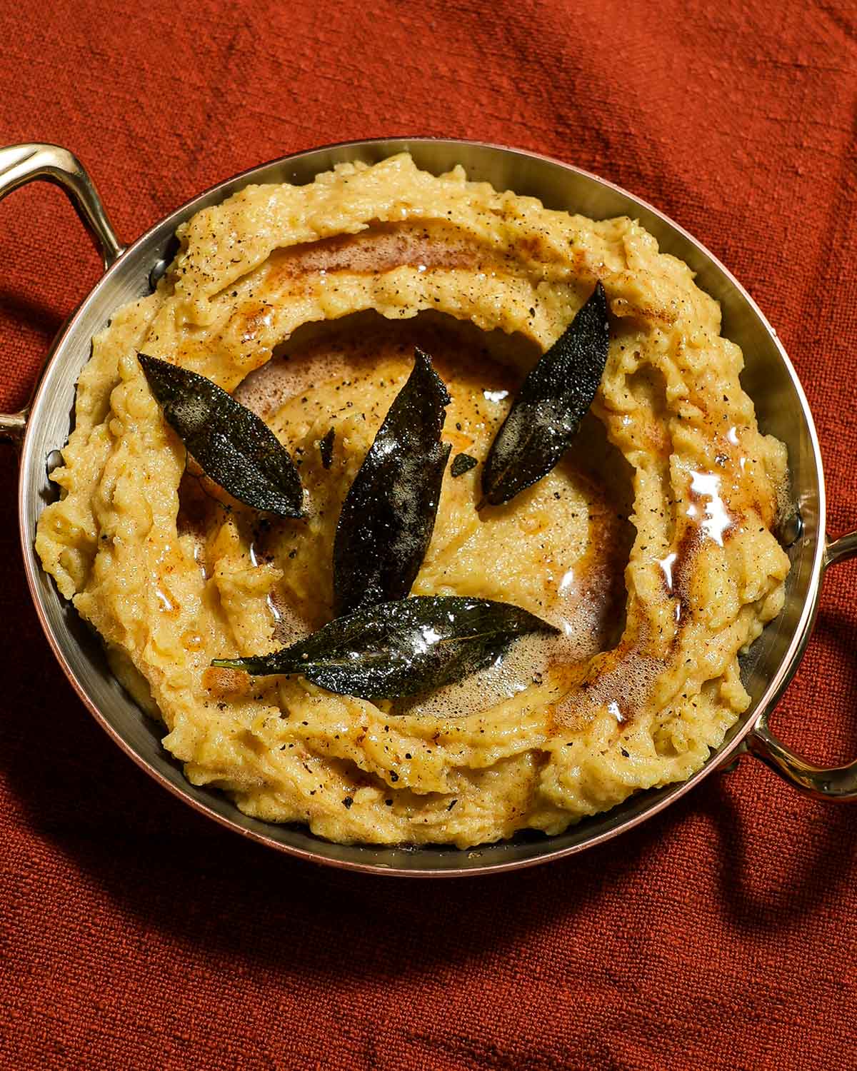 A bowl plated of brown butter mashed potatoes and sage.