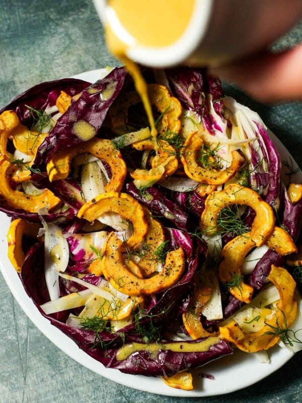 A platter of delicata squash salad with fennel and radicchio with dressing being poured over.