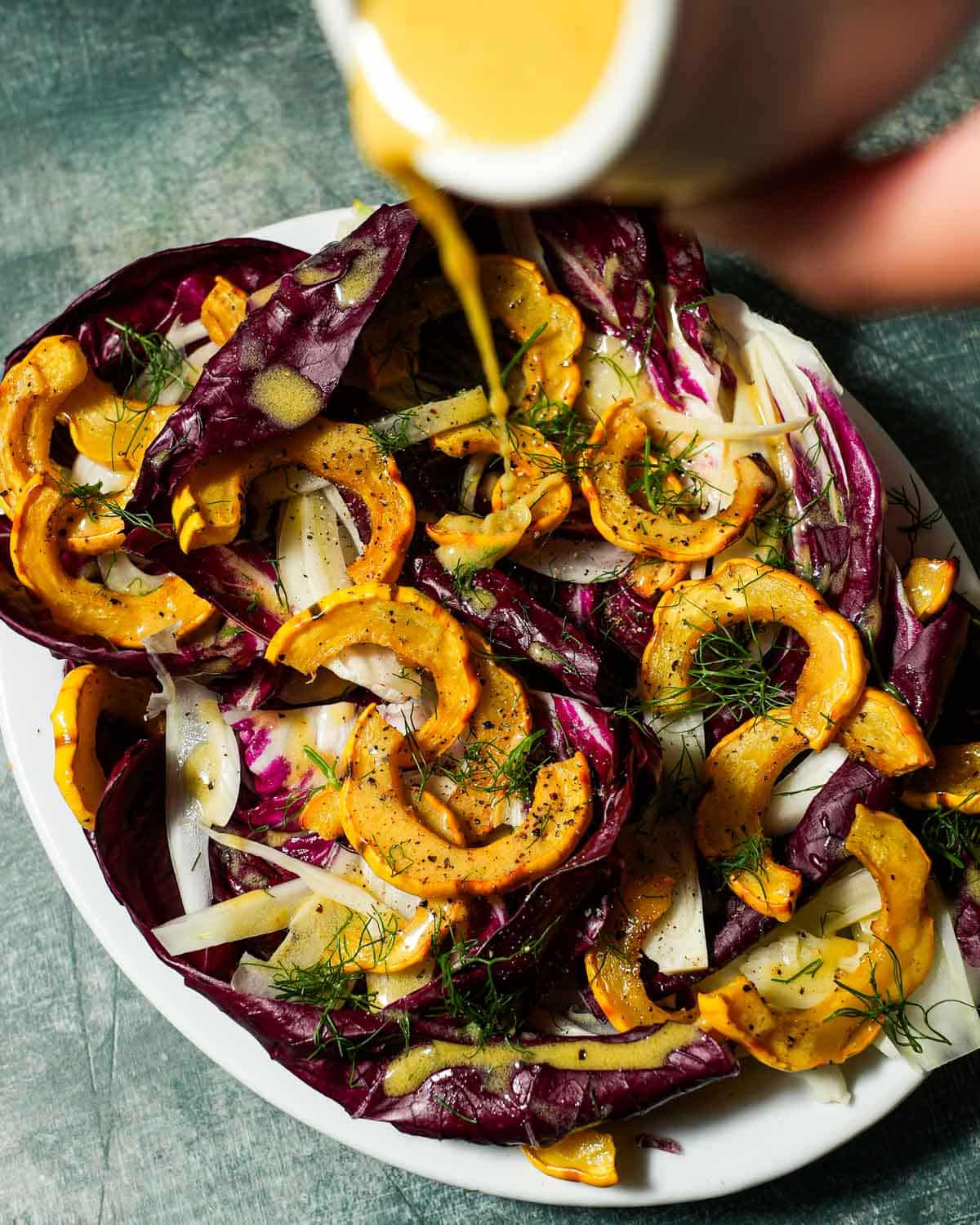 A platter of delicata squash salad with fennel and radicchio with dressing being poured over.