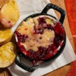 A baking dish of melty baked brie cheese with cranberry sauce.