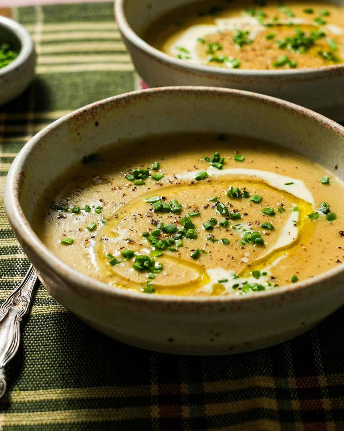 Potato leek soup with chives and a spoon on a plaid tablecloth.