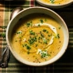 A bowl of creamy potato leek soup on a plaid tablecloth.