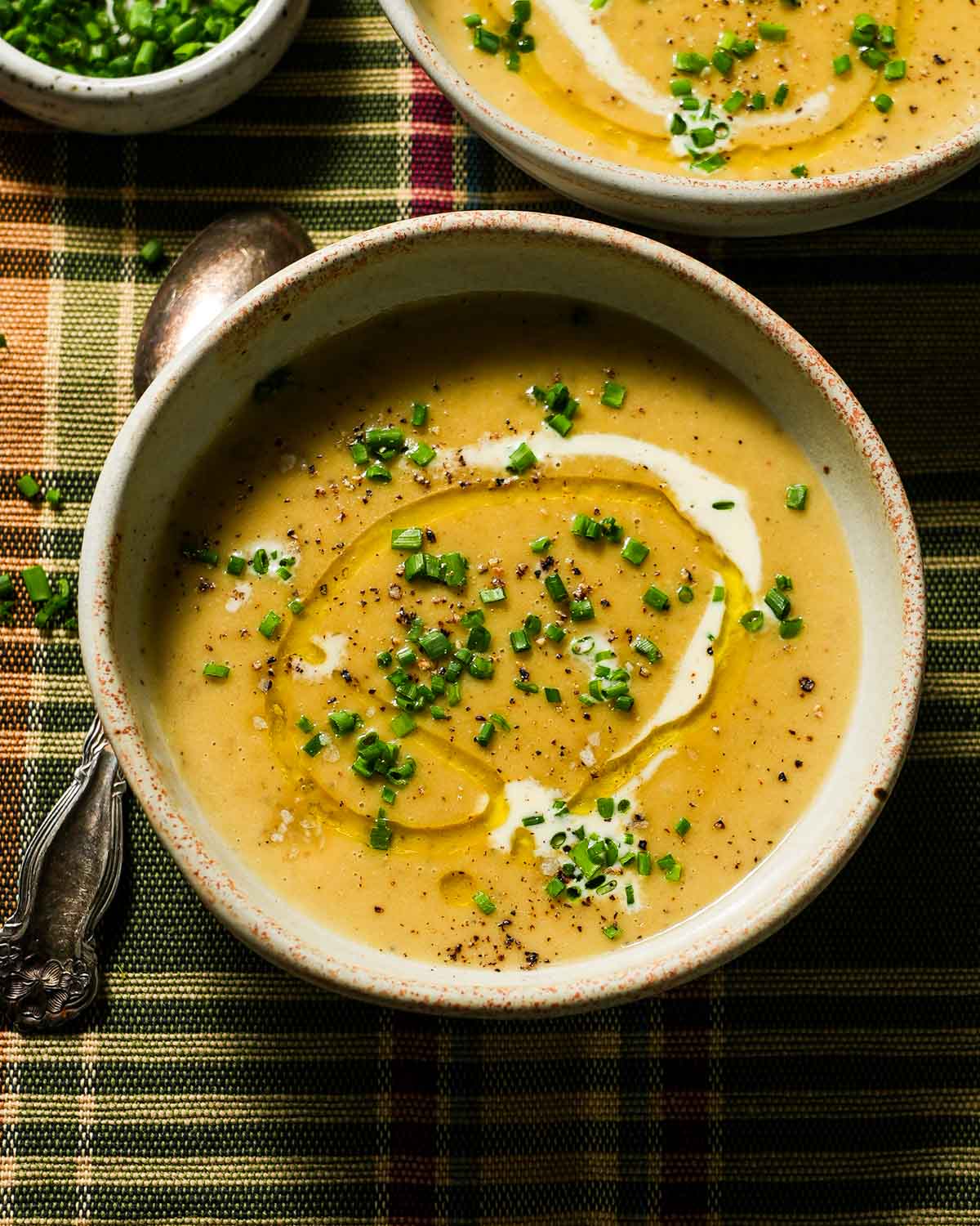 2 bowls of creamy potato leek soup on a plaid tablecloth.