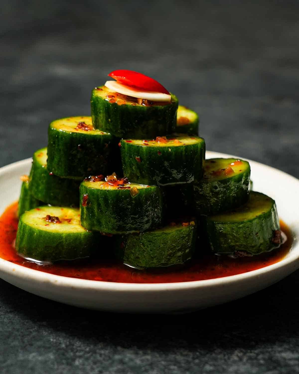 Cucumbers stacked on a plate in a pyramid formation with a garlic and bell pepper.