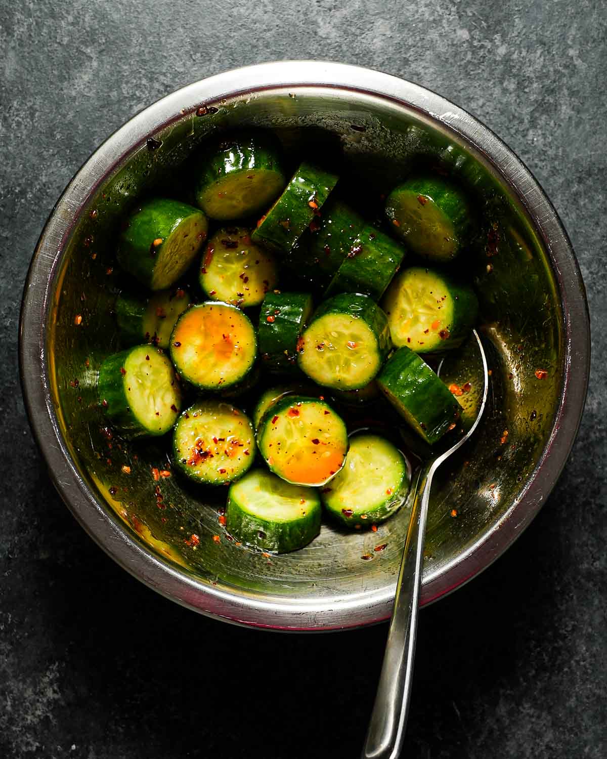 Sliced Persian cucumbers being tossed with a spicy vinegar dressing.