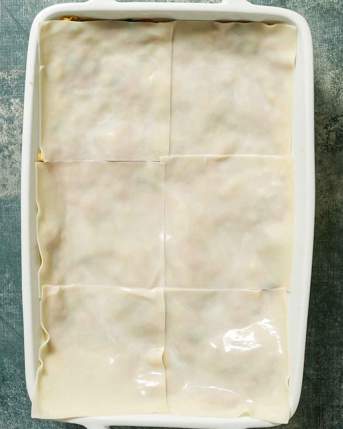 A baking pan layered with wonton wrappers and pork filling about to be steamed.