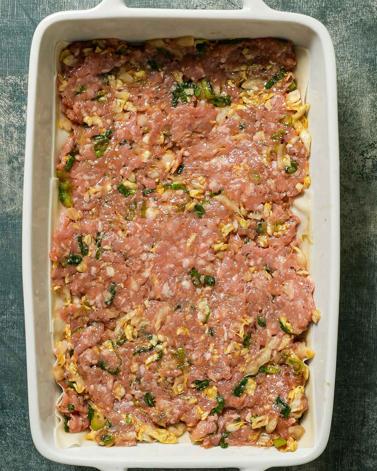 A baking pan layered with wonton wrappers and pork filling.