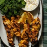 A platter of grilled yogurt marinated chicken with a charred lemon, yogurt and herbs.
