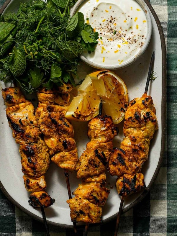 A platter of grilled yogurt marinated chicken with a charred lemon, yogurt and herbs.