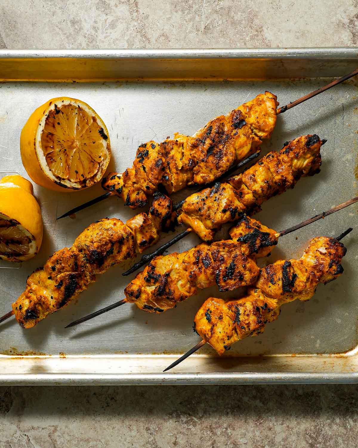 Grilled skewers on a sheet pan with charred lemon.
