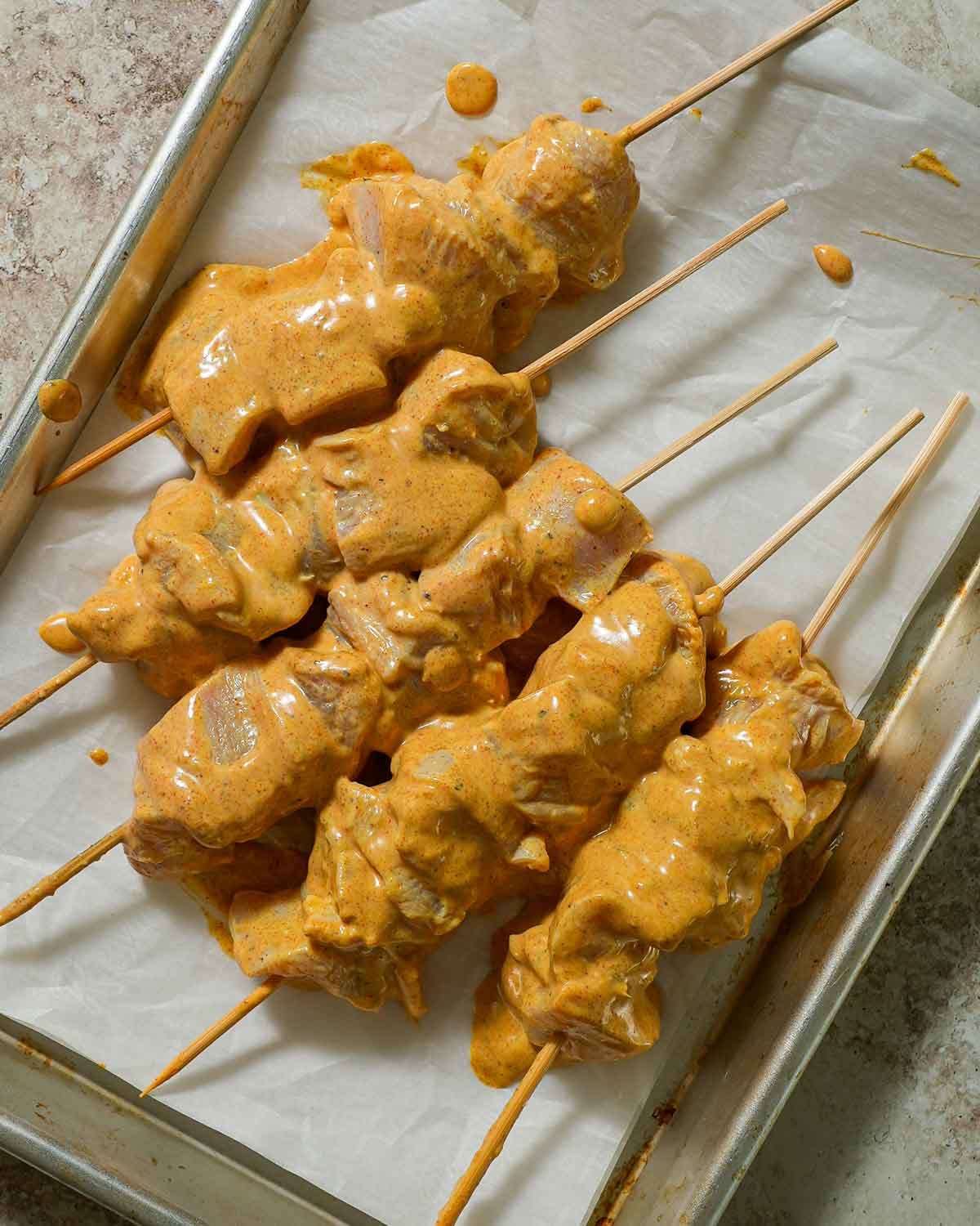 Yogurt marinated skewers on baking sheet with parchment paper.