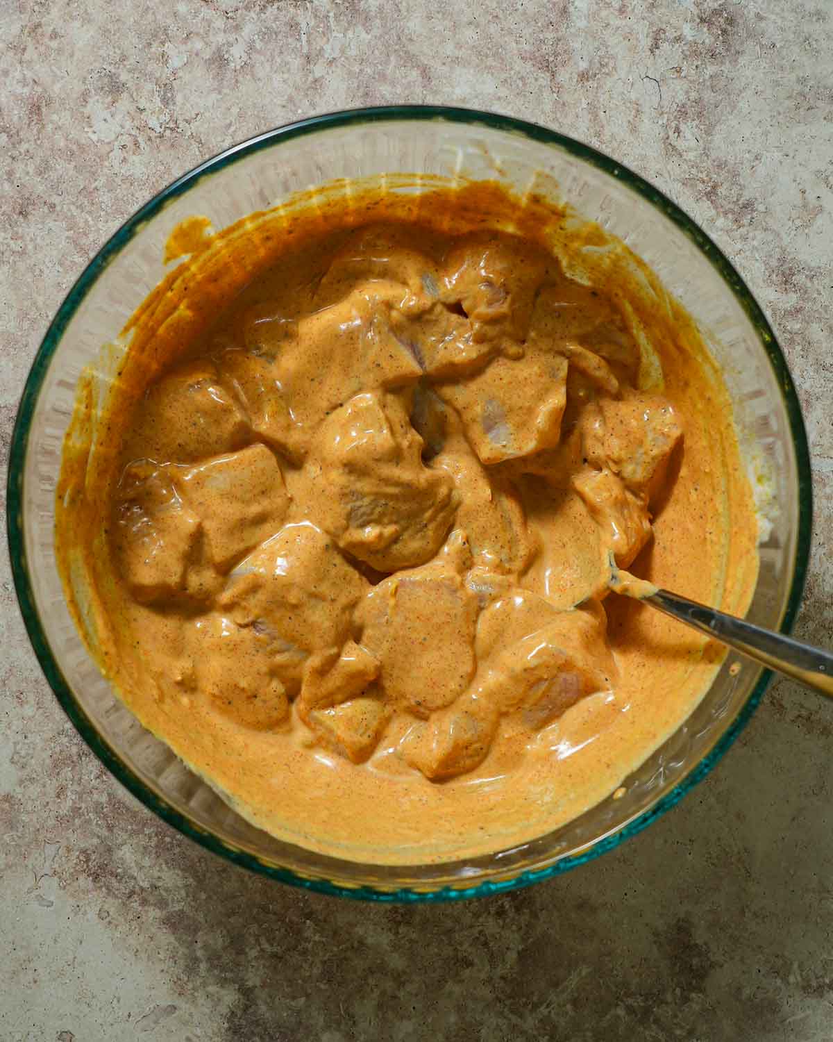 A bowl of chicken tossed in a spiced yogurt marinade with a spoon.
