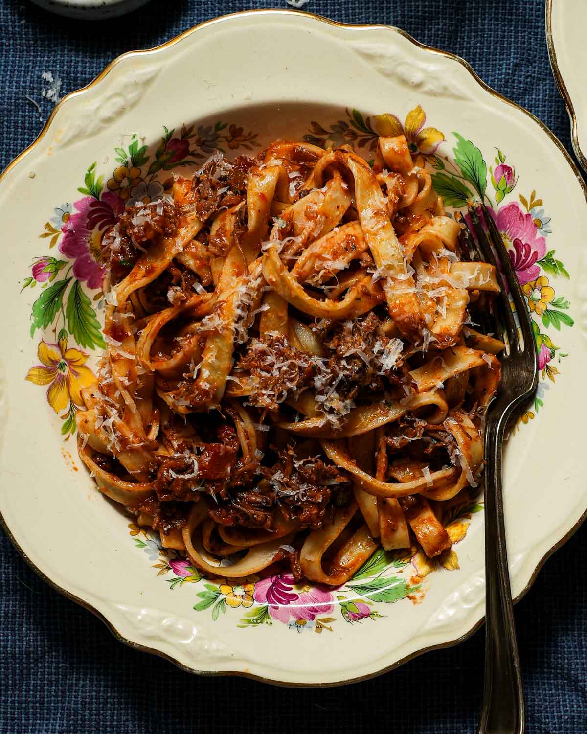 A floral bowl with pasta and ragu sauce with a fork.