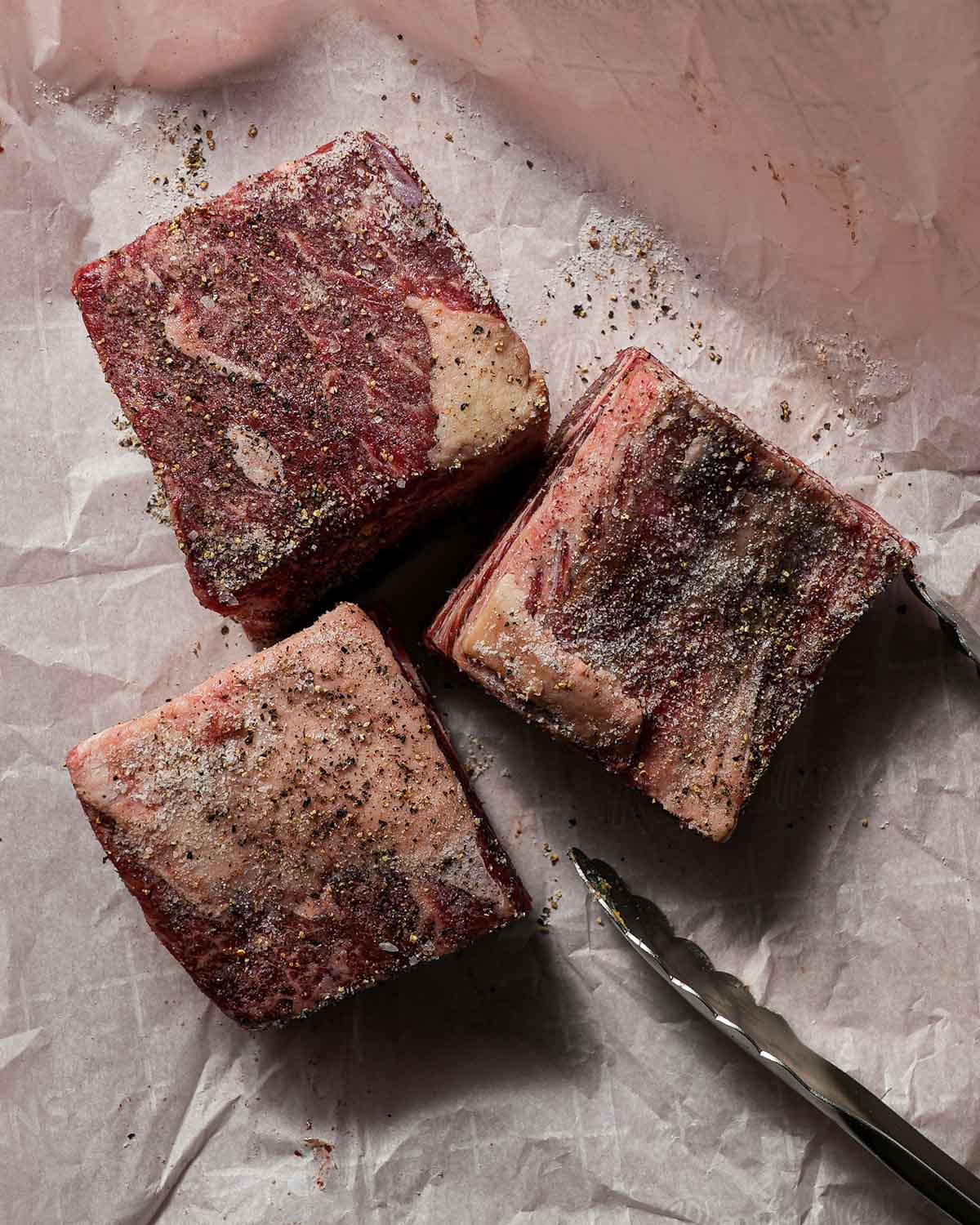 3 pieces of bone-in short rib on parchment paper with salt and pepper.