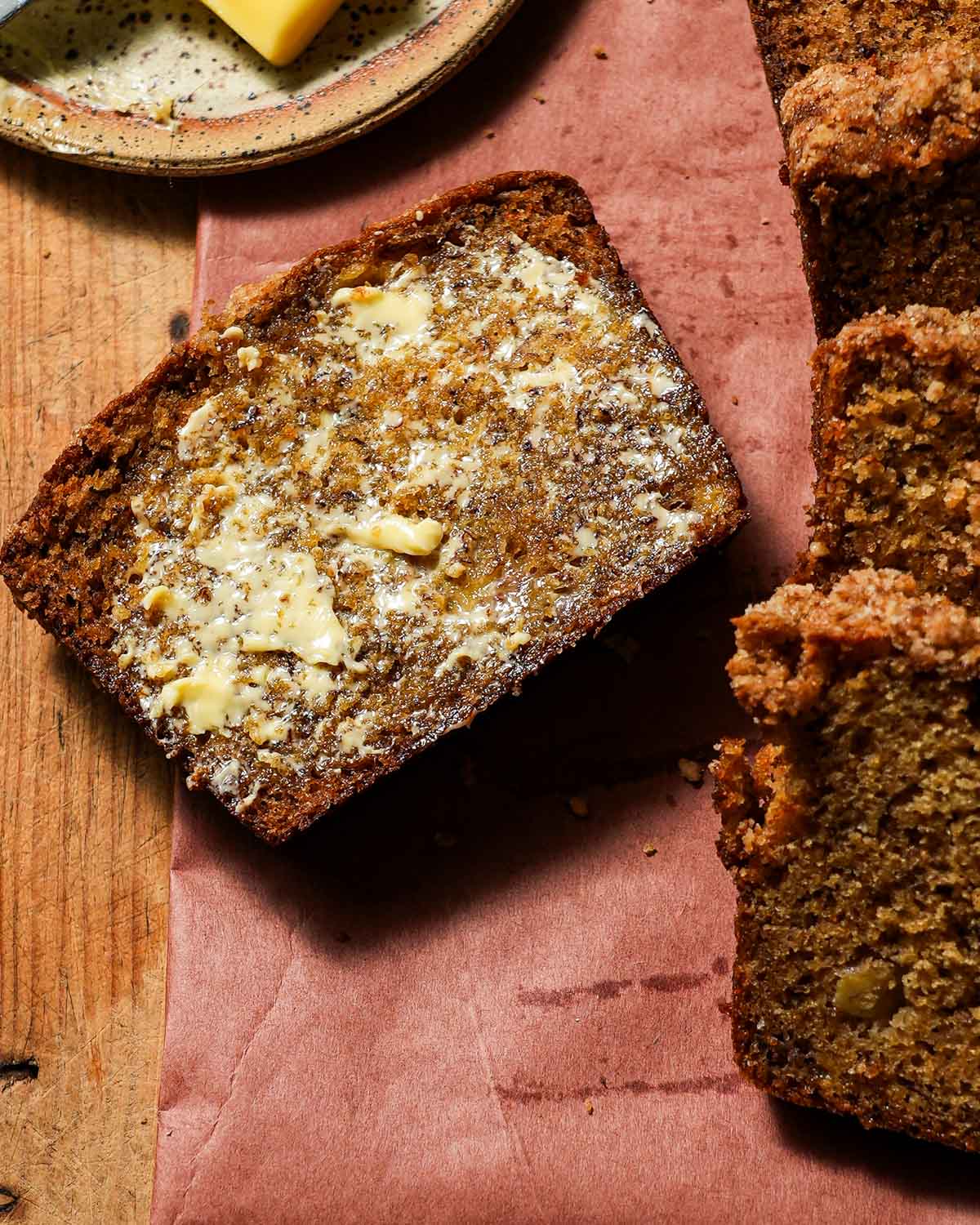 A slice of brown butter banana bread on a cutting board with butter spread on it.