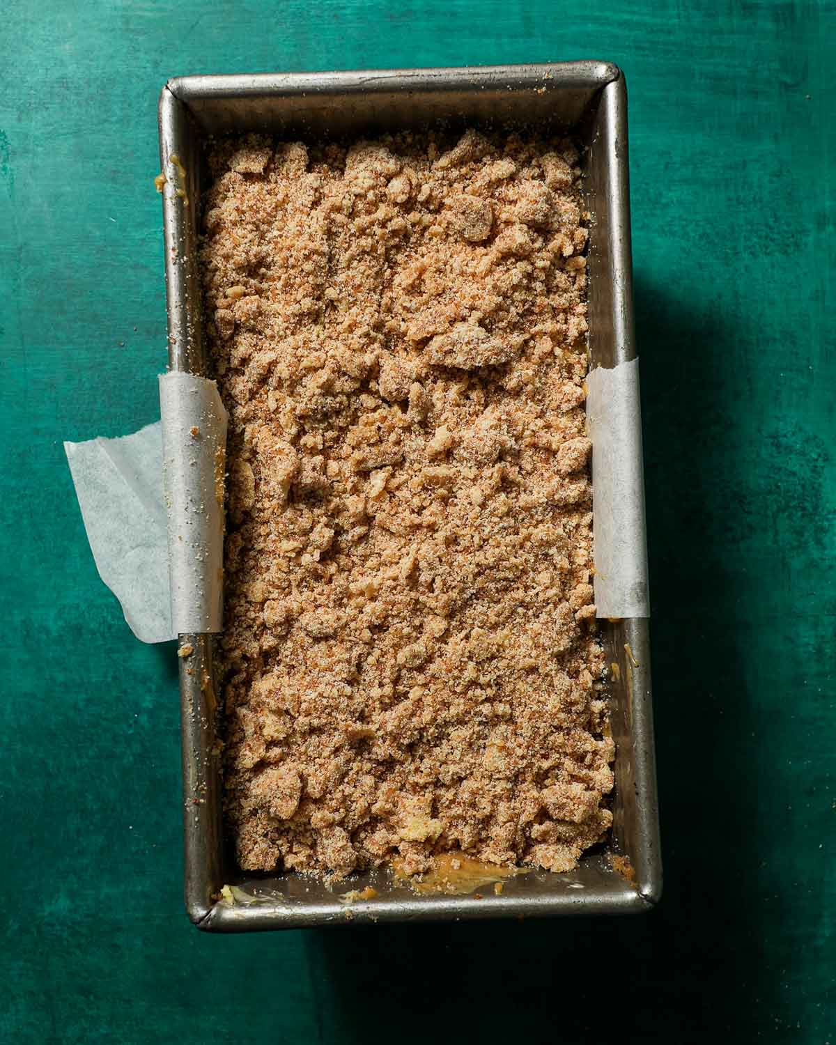 A loaf pan with brown butter banana bread batter topped with streusel before baking.