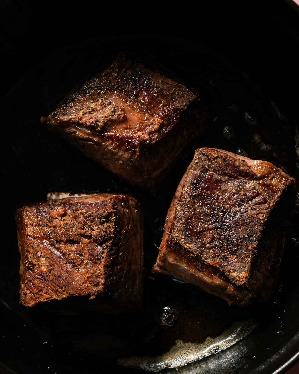 A dutch oven with seared short ribs ready to be braised.