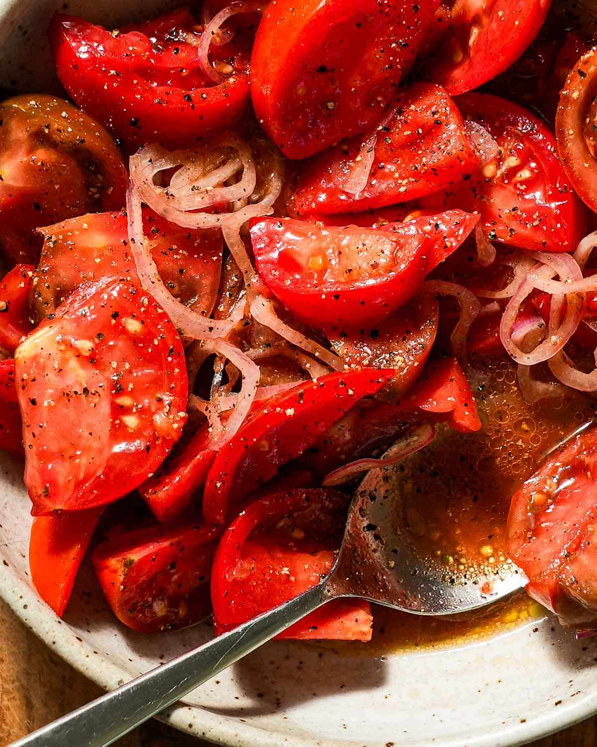 A bowl of marinated tomatoes with a spoon showing the juices.