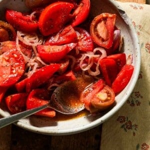 A bowl of marinated tomatoes with a spoon of juices.
