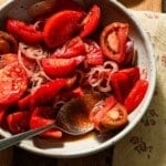 A bowl of marinated tomatoes with a spoon of juices.