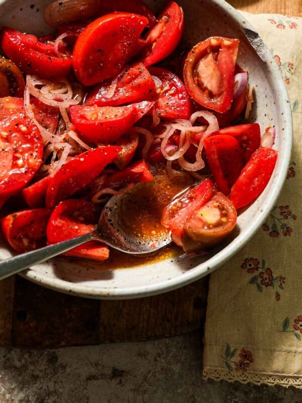 A bowl of marinated tomatoes with a spoon of juices.