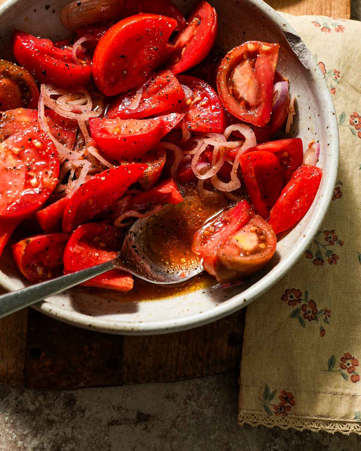 A bowl of marinated tomatoes with a spoon of juices.