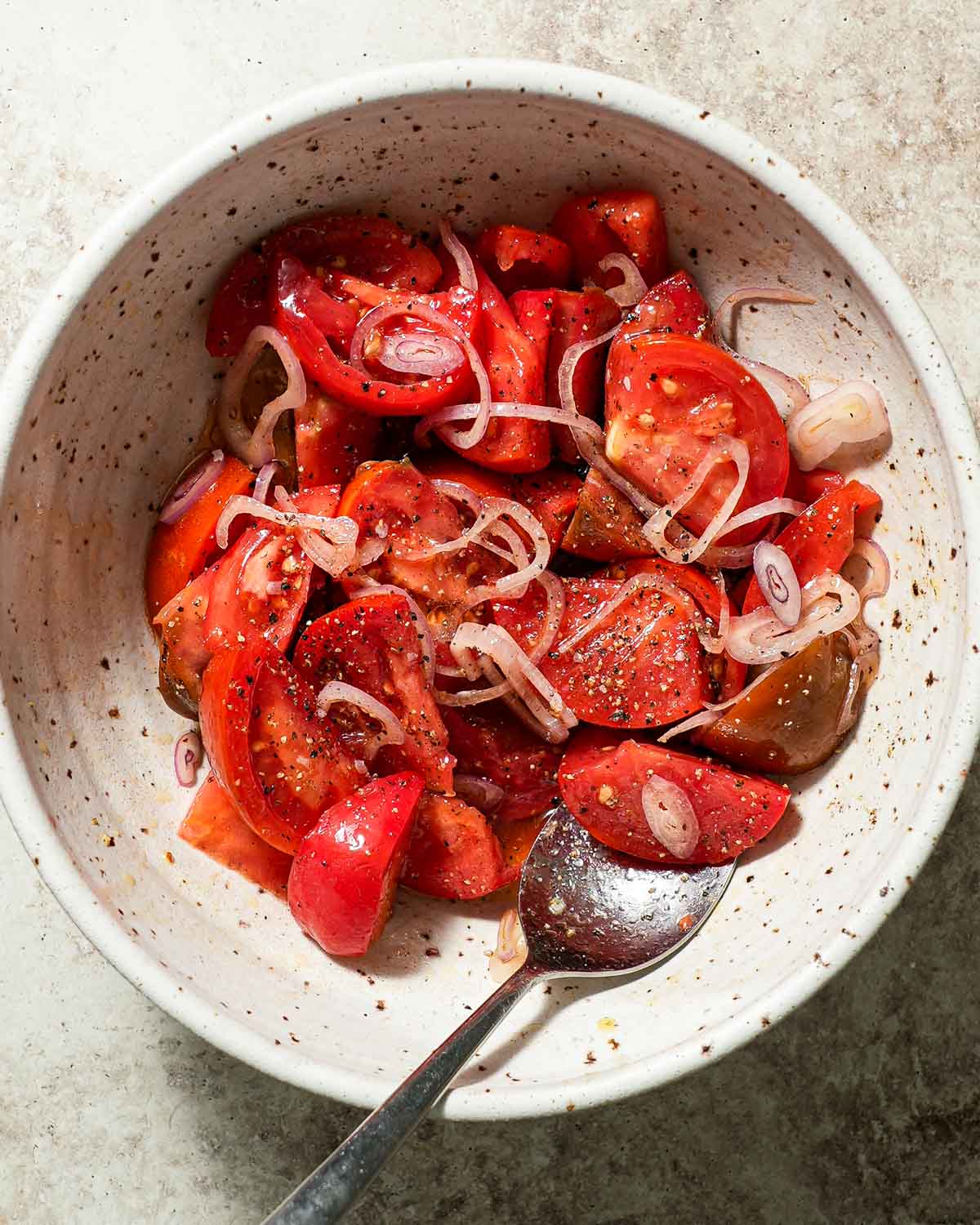 A bowl of quartered tomatoes with shallots being tossed with vinegar and olive oil.