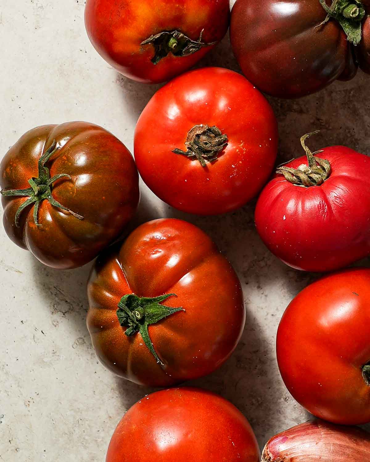 A bunch of heirloom tomatoes and shallots scattered next to each other.