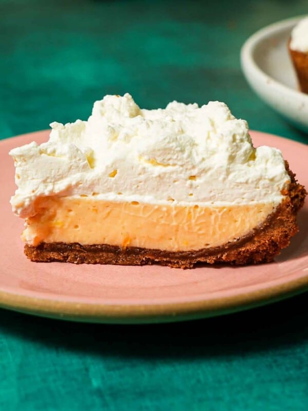 A pink plate with a Meyer lemon pie slice topped with whipped cream.